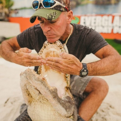 Person displays open mouth of large crocodile outdoors.